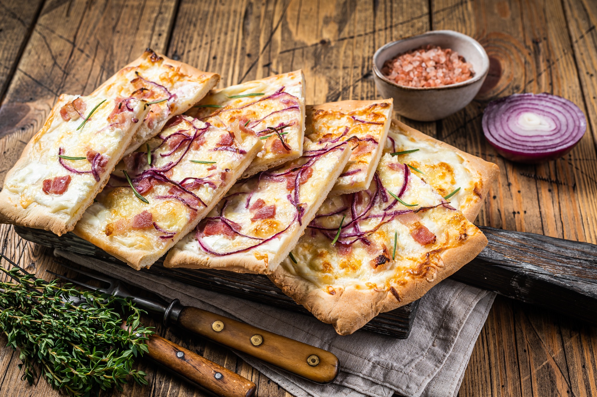 Flammkuchen or tarte flambee with cream cheese, bacon and onions. Wooden background. Top view