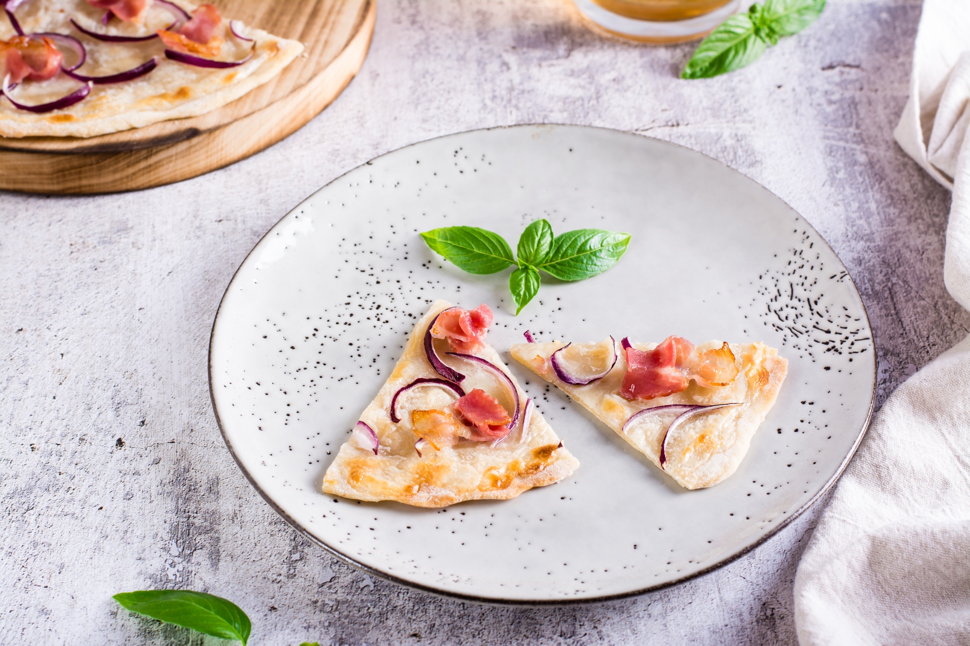 Slices French tarte flammkuchen with bacon, cream cheese and onion on a plate.